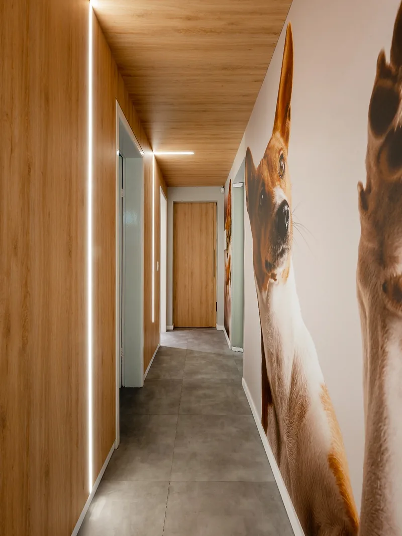 Corredor com forro em madeira, iluminação linear embutida e painel fotográfico de piso a teto.