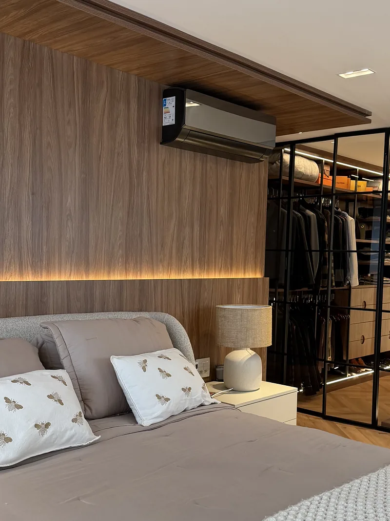 Dormitório com cabeceira em madeira ripada, iluminação embutida e closet integrado.