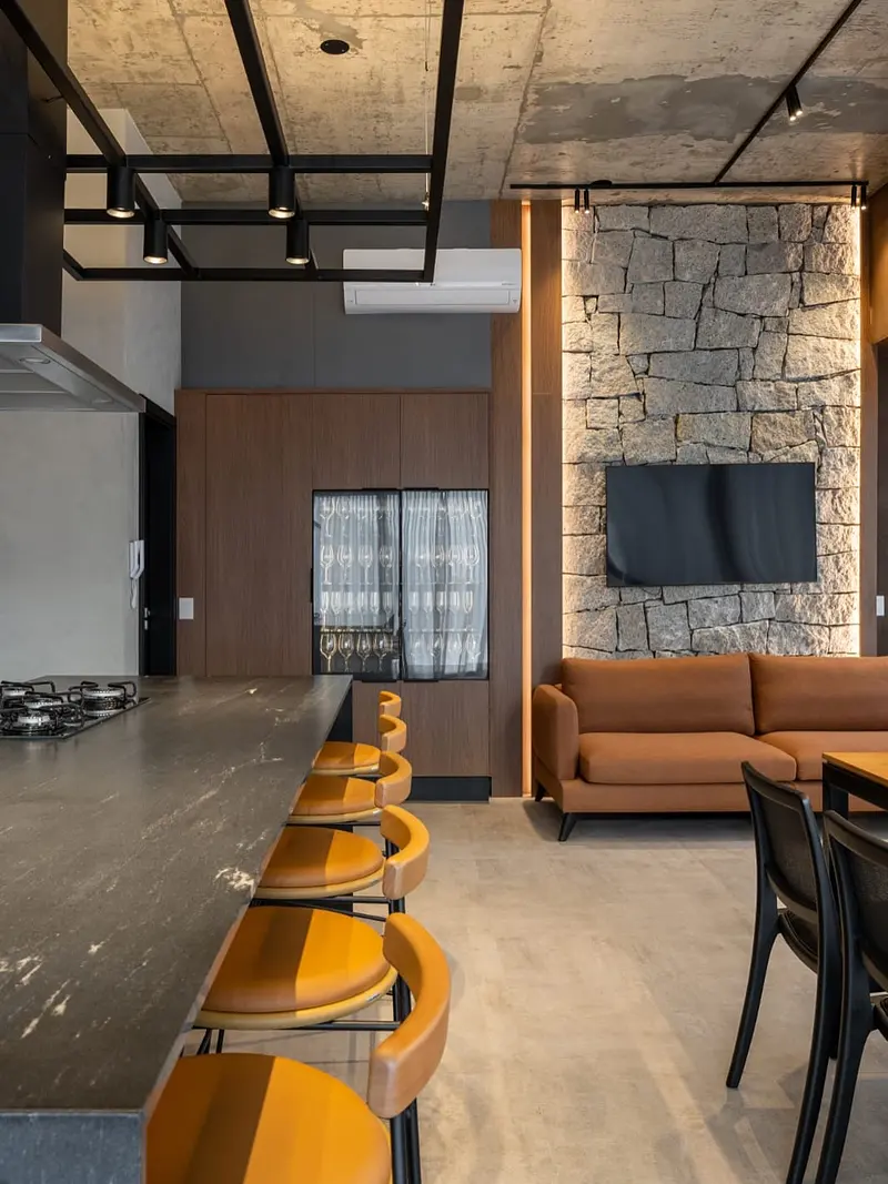 Ambiente gourmet com parede em pedra, estrutura metálica preta e banquetas.