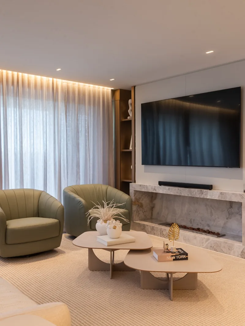 Living com lareira em mármore, painel de TV, poltronas verdes e cortina em linho.