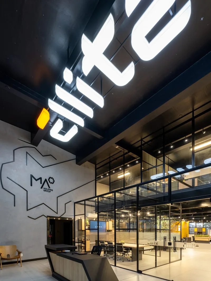 Recepção corporativa com letreiro em neon, mezanino e salas envidraçadas.