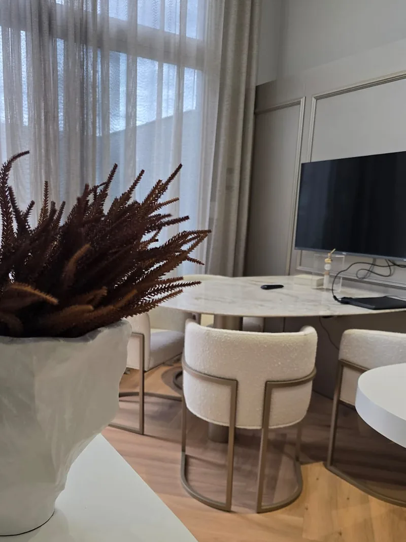 Sala de jantar com mesa redonda em mármore, cadeiras estofadas e pé-direito duplo.